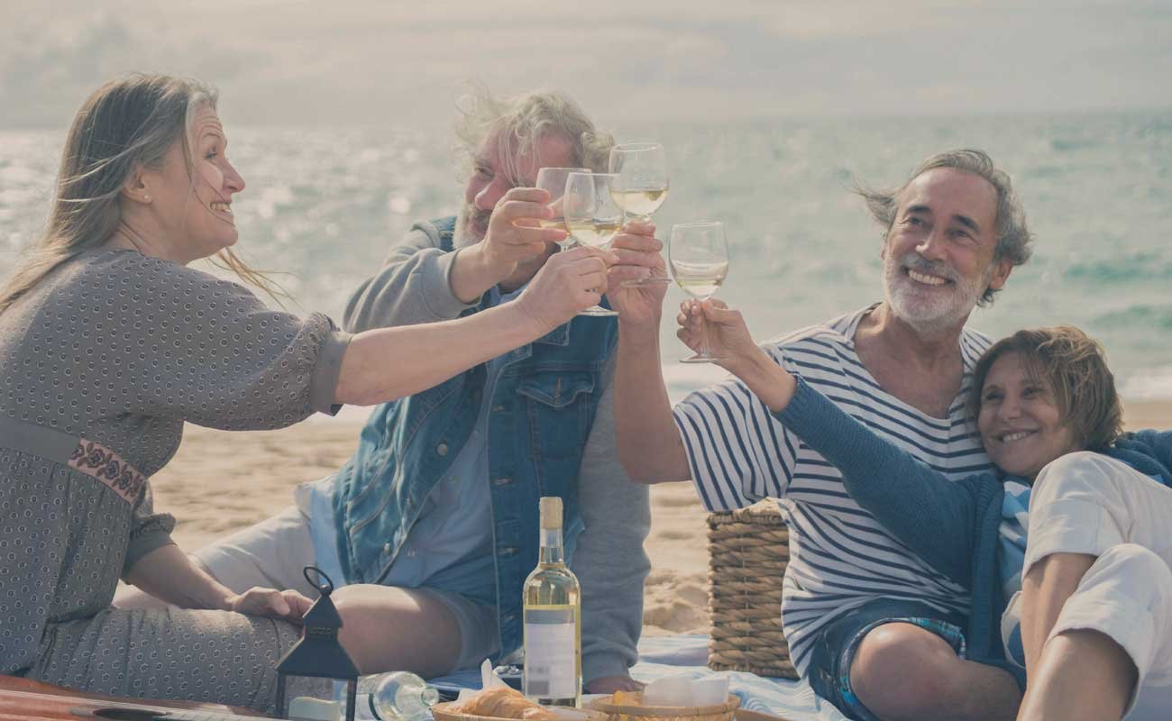 Two older couples raising their wine glasses to cheers on the beach. kelowna cruise